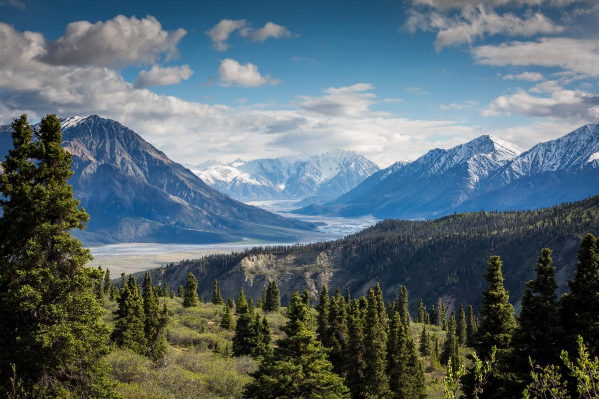 A mountainous region with multiple peaks and valleys, lush greenery, and blue skies