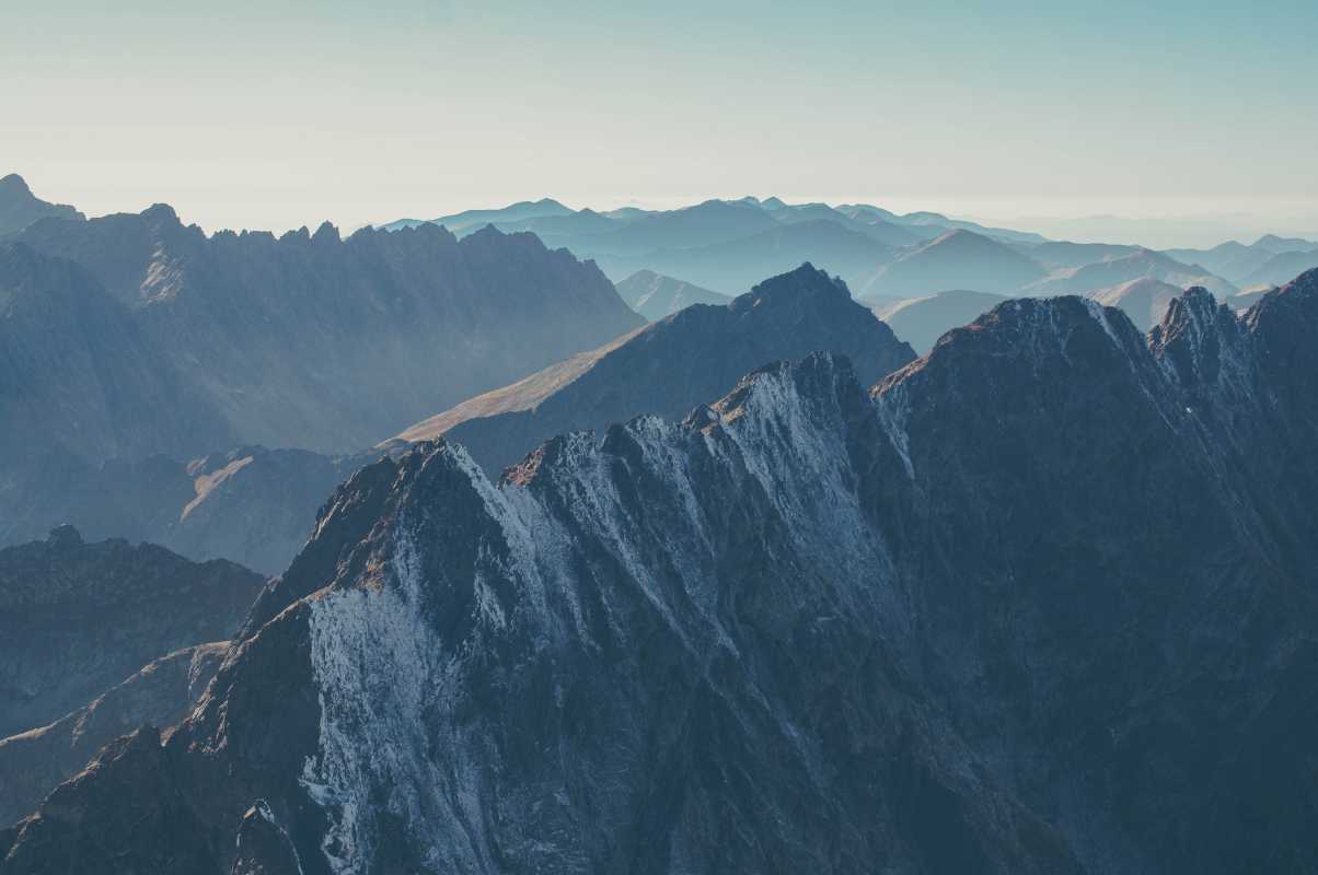 Steep, snowy mountains with a hazy blue sky above them.