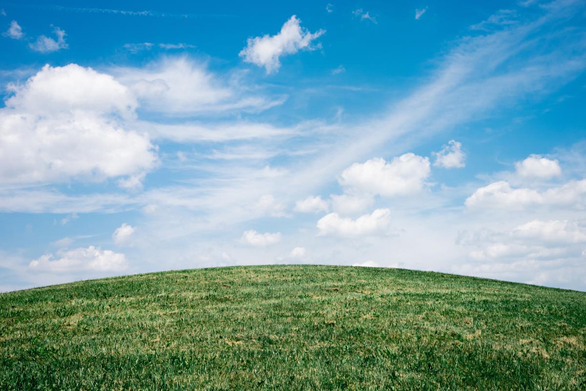 A grassy green knoll with slightly cloudy blue skies above.