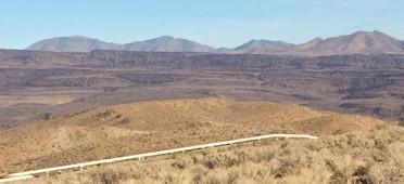 Looking east over a Coso geothermal field pipeline to dark brown, faulted and incised lava flows. 