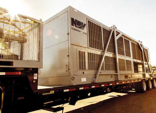 Wide shot of the Tundra Max skid and trailer beside a drilling rig, with visible hoses connected to the mud system, fans or heat exchangers clearly in view, and workers in standard PPE to convey scale and real-world deployment.