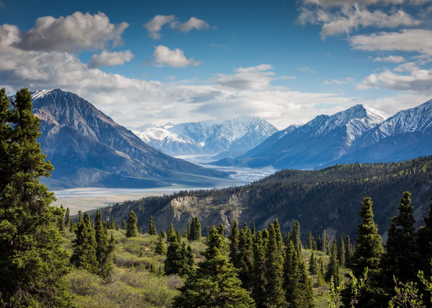 A mountainous region with multiple peaks and valleys, lush greenery, and blue skies