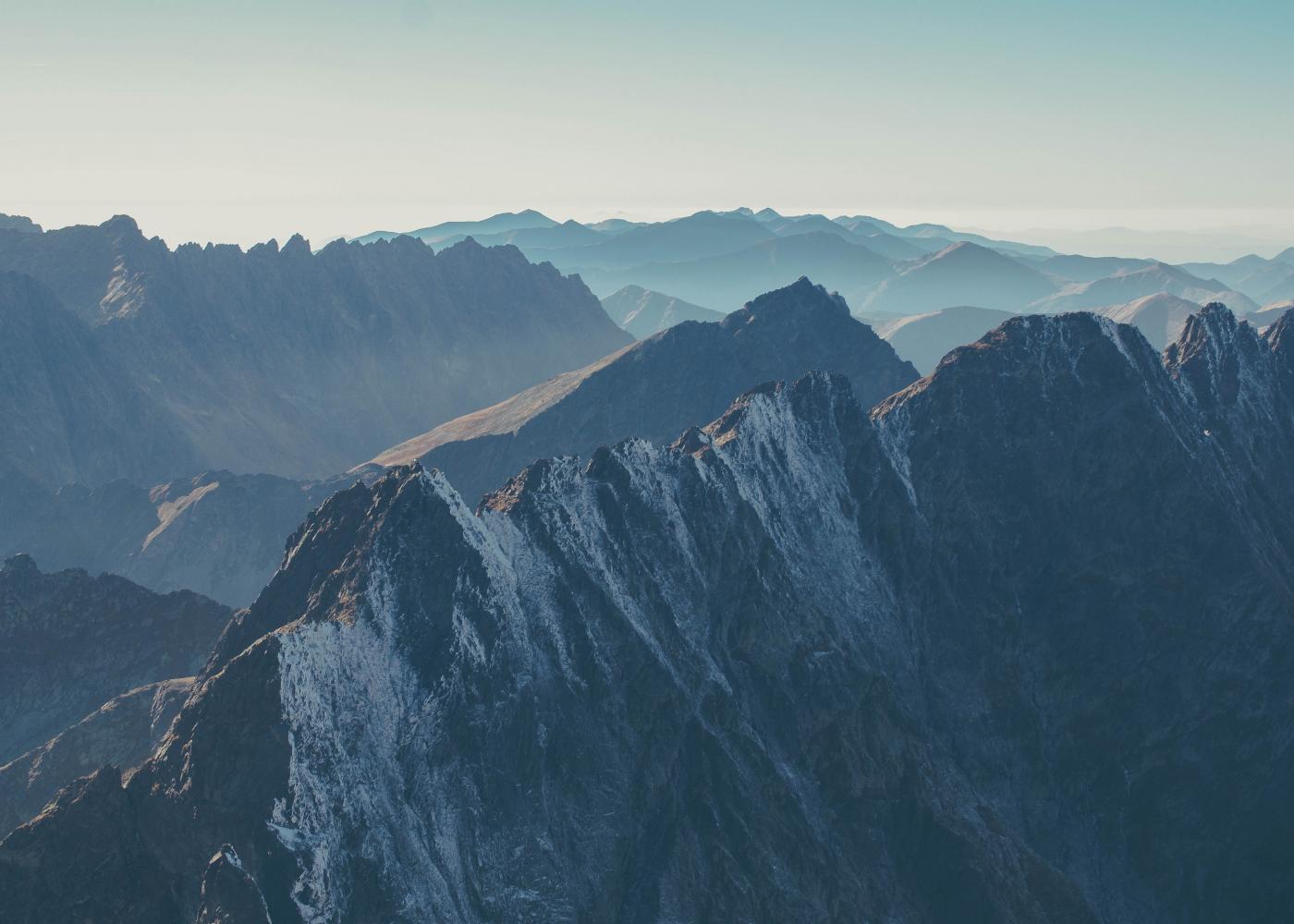 Steep, snowy mountains with a hazy blue sky above them.