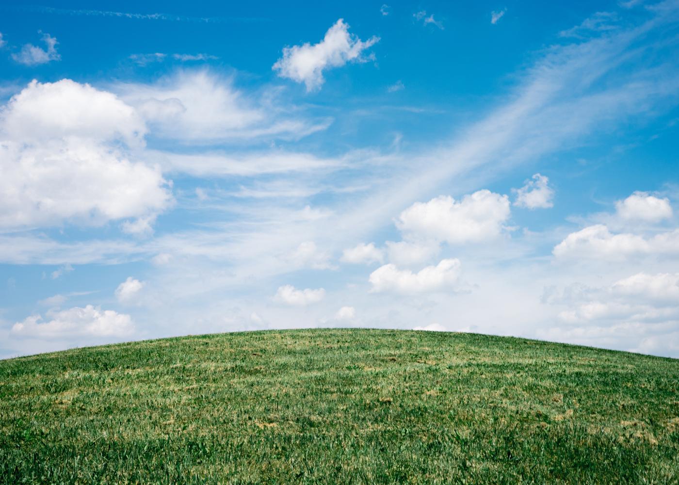 A grassy green knoll with slightly cloudy blue skies above.