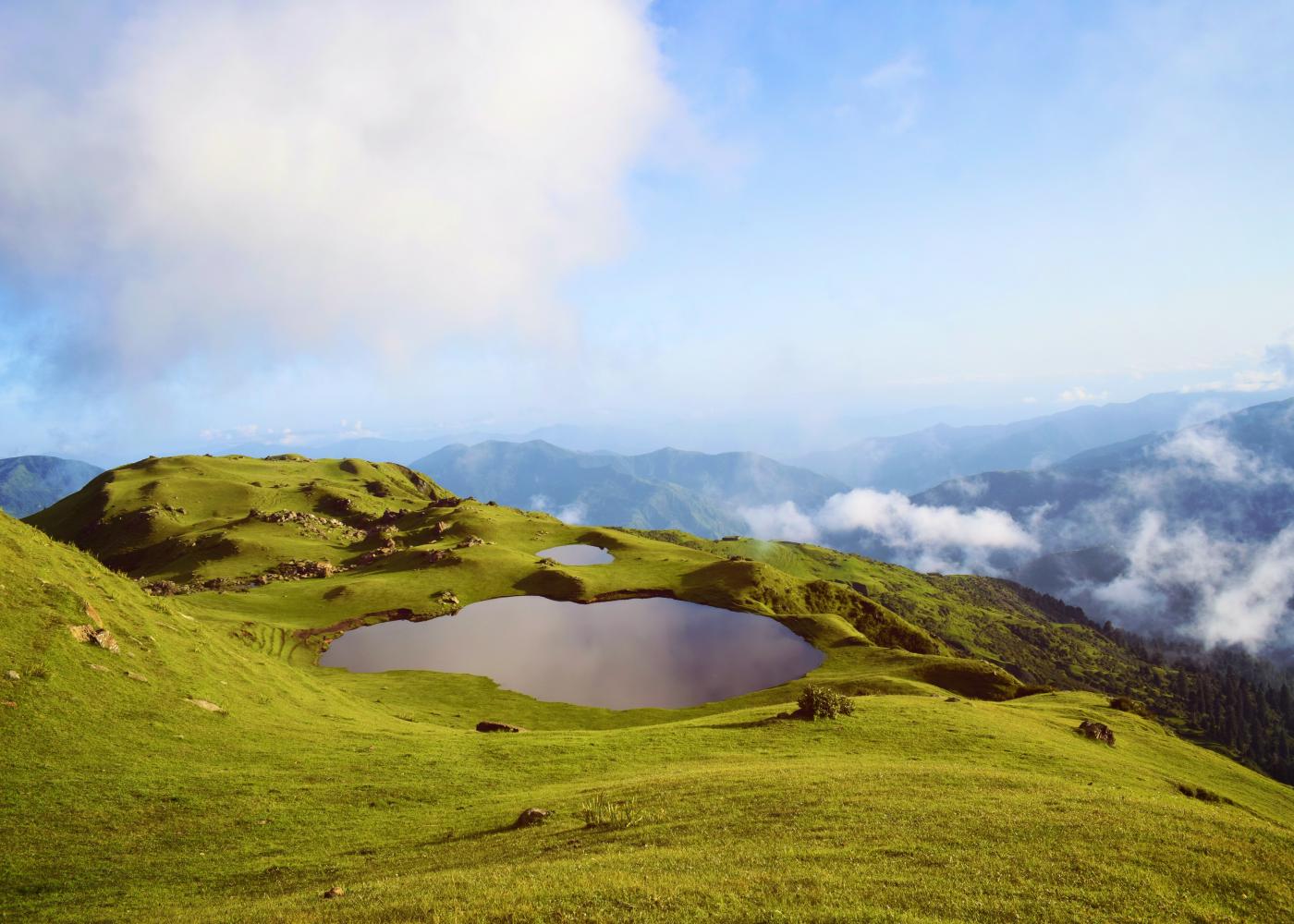 Mountains with a small pond inside of it with larger mountains in the background and cloudy skies above.