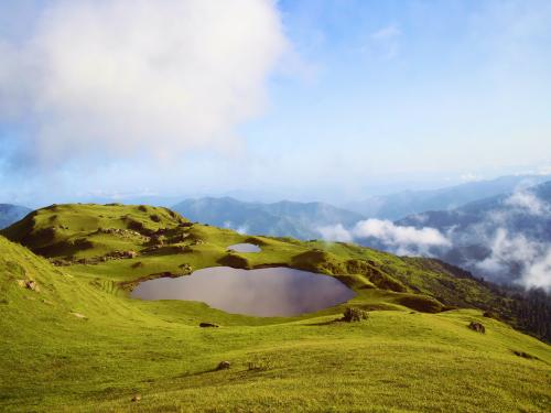 Mountains with a small pond inside of it with larger mountains in the background and cloudy skies above.